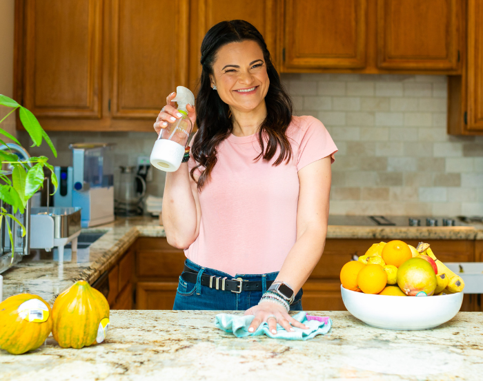 Leticia Oliveira holding a household spray bottle beside fresh produce